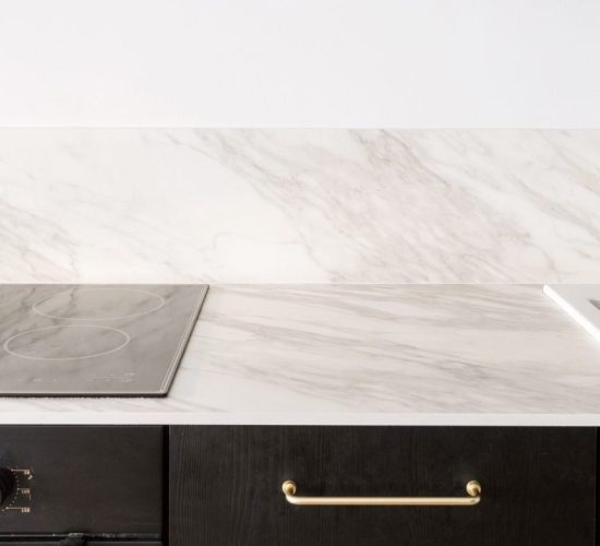 luxury interior at home kitchen, new wooden cupboard, electric oven, induction hob on marble countertop, white sink, water faucet and cooker hood